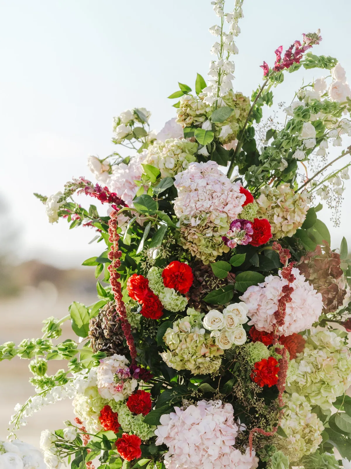 A tall arrangement of red, white, and green florals outdoors
