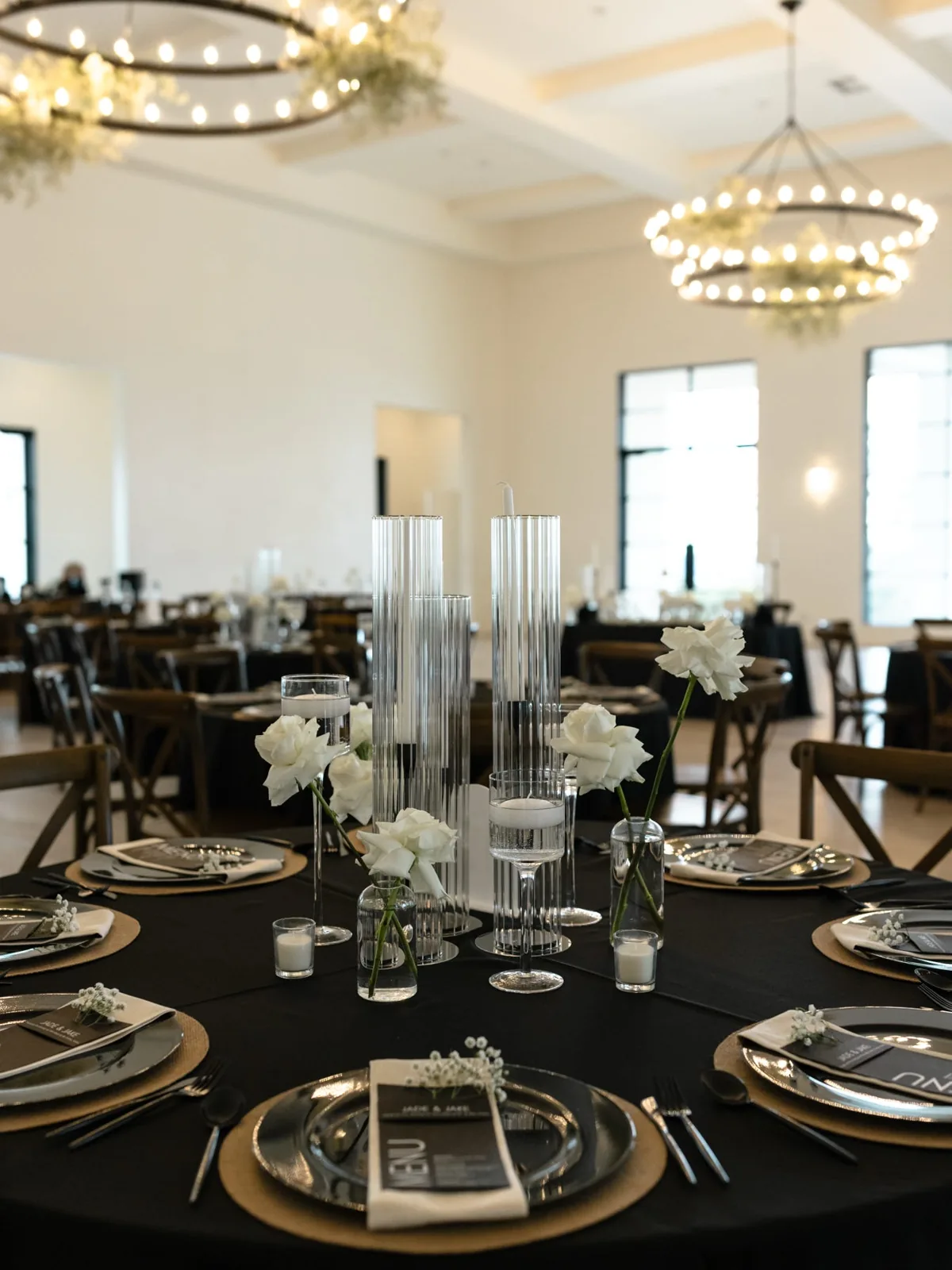 Reception hall set with black linens, gold chargers, and ring chandeliers